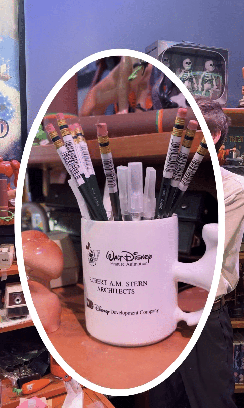 White mug shaped pencil holder filled with pencils and markers labeled Walt Disney Feature Animation and Robert AM Stern Architects on a toy shop shelf