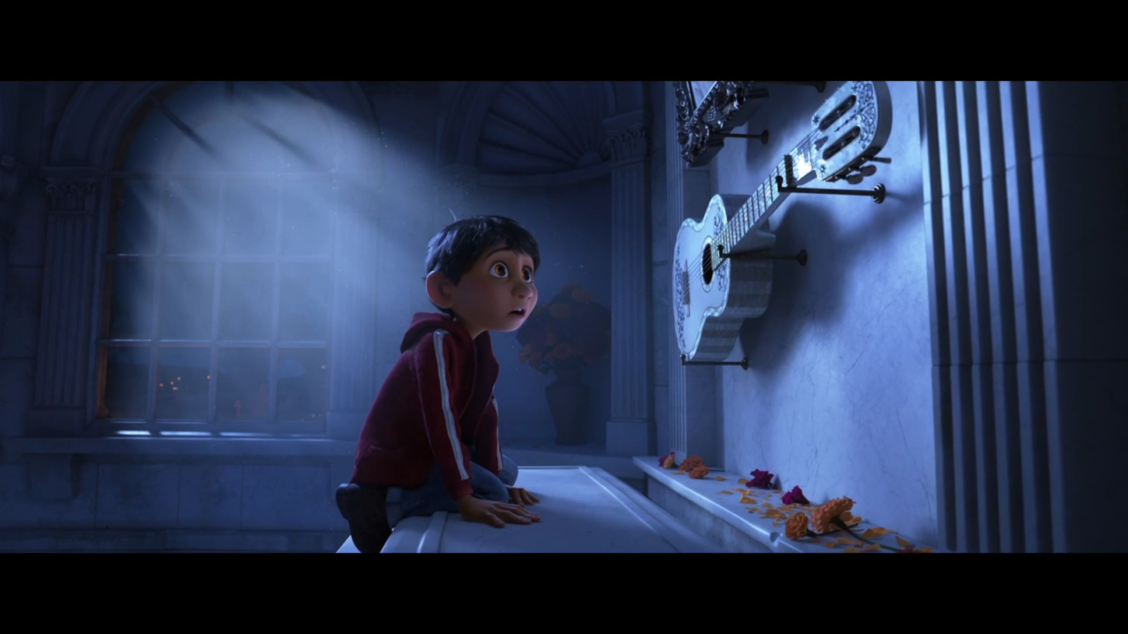 A young boy in a red hoodie kneels on a marble surface gazing at an ornate guitar mounted on a blue wall in a dim cathedral like room with flower petals scattered nearby
