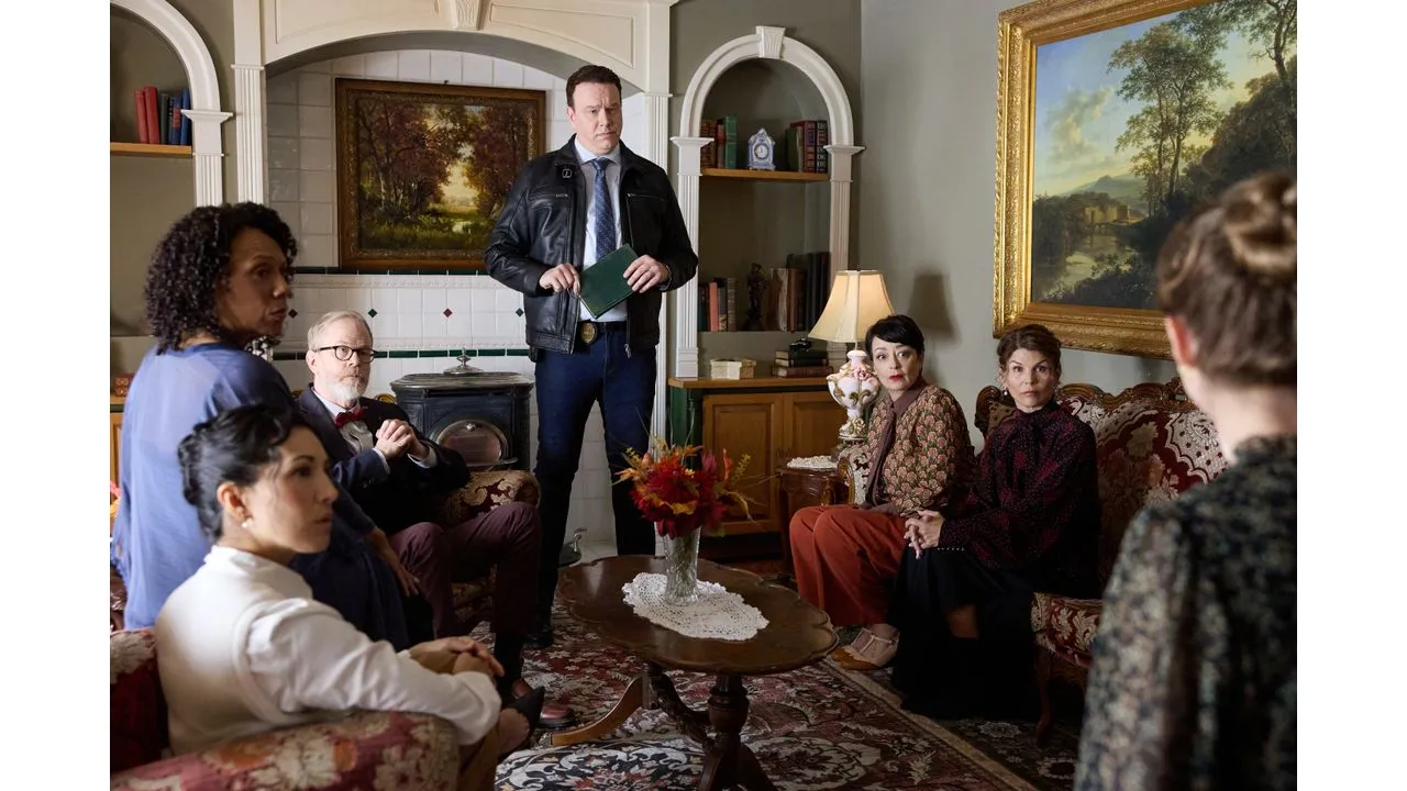 gsmk3 Fantasy Land News Group of six adults seated in a vintage living room listening as a man in a leather jacket stands with a notebook suggesting a tense discussion or interrogation