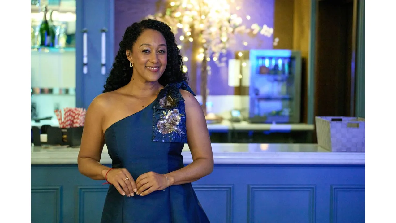 hhm2 Fantasy Land News Smiling woman in a dark blue one shoulder evening dress standing at a bar with a decorative sequin floral embellishment on the strap