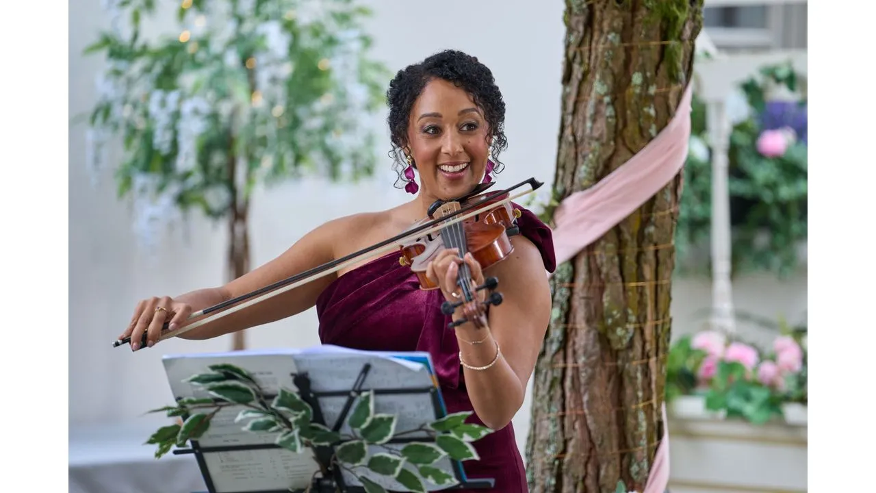 hhm3 Fantasy Land News Woman in a burgundy dress playing the violin outdoors reading sheet music on a stand beside a tree