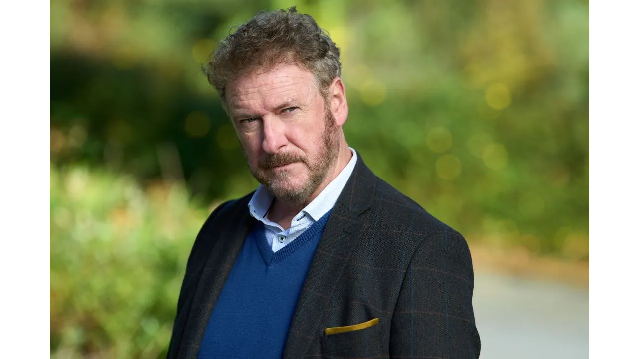 hhm4 Fantasy Land News Portrait of a middle aged man with a beard wearing a navy blue sweater and dark blazer standing outdoors with a blurred green background