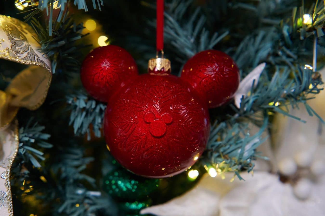 Red glass Christmas ornament with an embossed floral pattern hanging from a Christmas tree branch