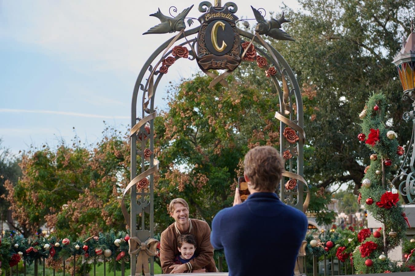 Family posing under an ornate metal arch decorated with roses and ribbons in a festive outdoor display nearby a Christmas tree