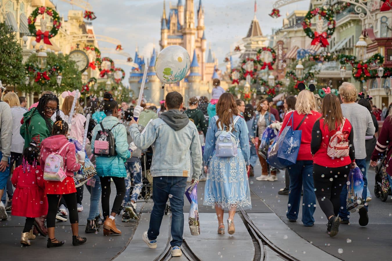 Crowded Disney park street during a holiday celebration with a castle in the background and confetti falling overhead