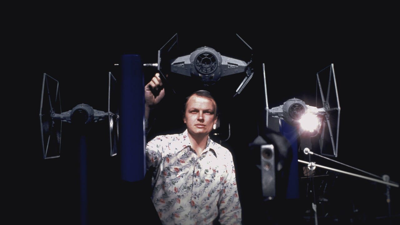 Man in a floral shirt posing among life size TIE fighter props in a dark studio backdrop