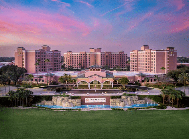 Pink resort hotel complex at sunset with a central entrance fountain and manicured lawn sign reads Caribe Royale in front