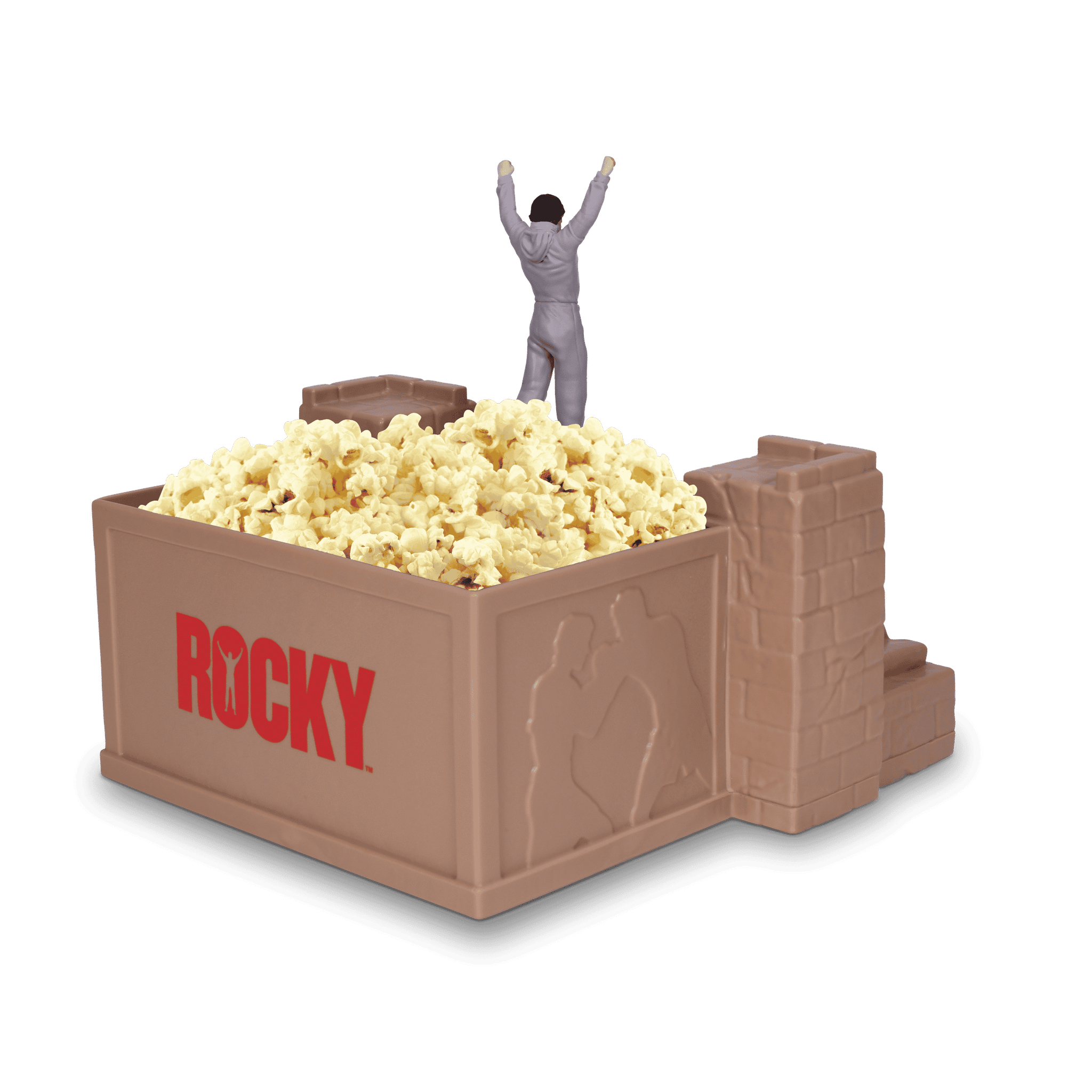 Man in a gray jumpsuit emerges from a large popcorn box with arms raised surrounded by popcorn and chocolate bars