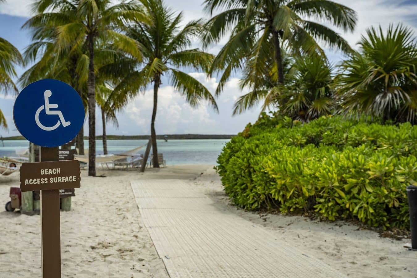 Blue wheelchair accessible sign on a sandy beach with a paved path to the ocean