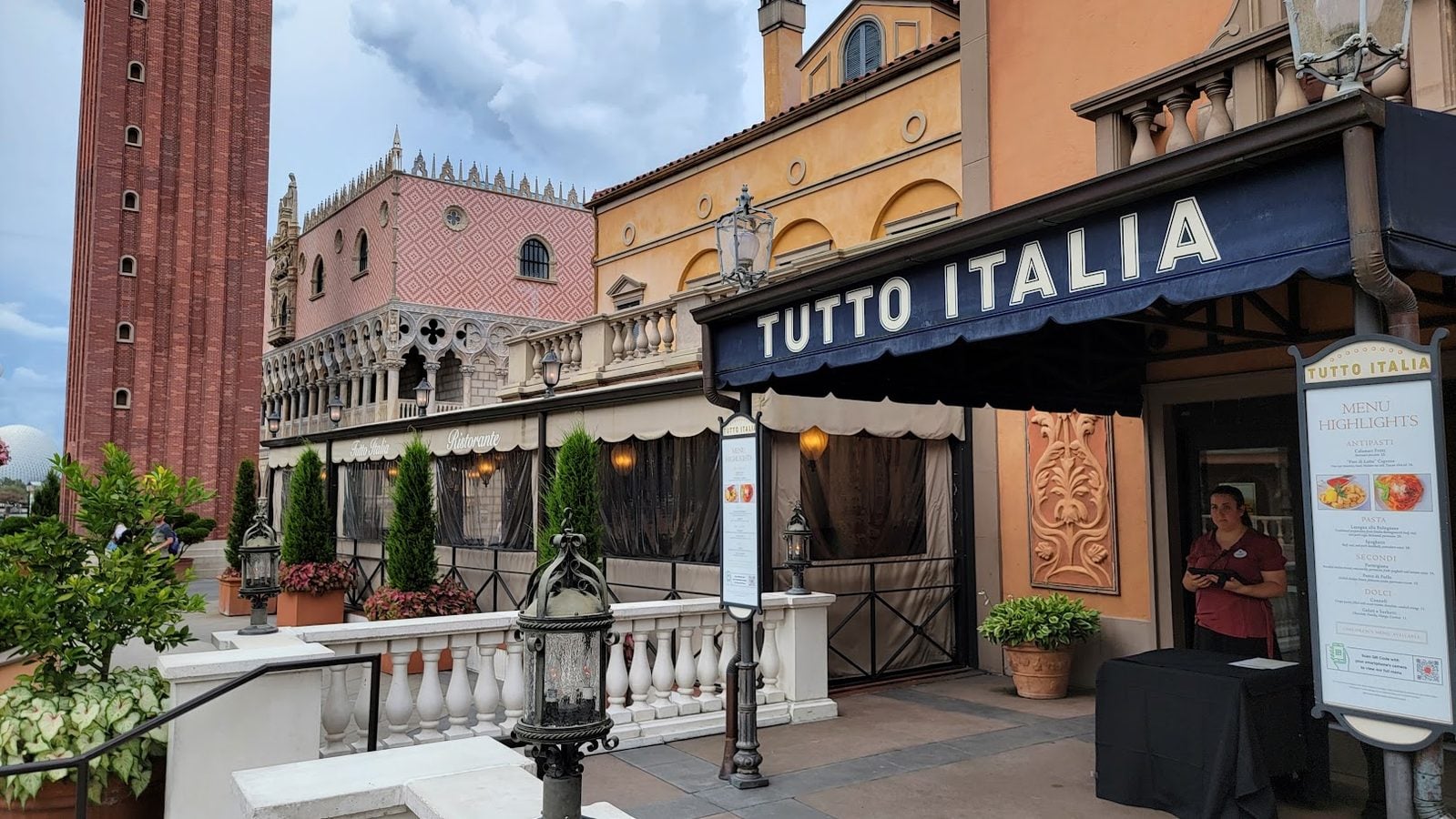 Exterior view of Tutt Italia restaurant with yellow orange facade blue awning reading TUTTO ITALIA and outdoor dining area
