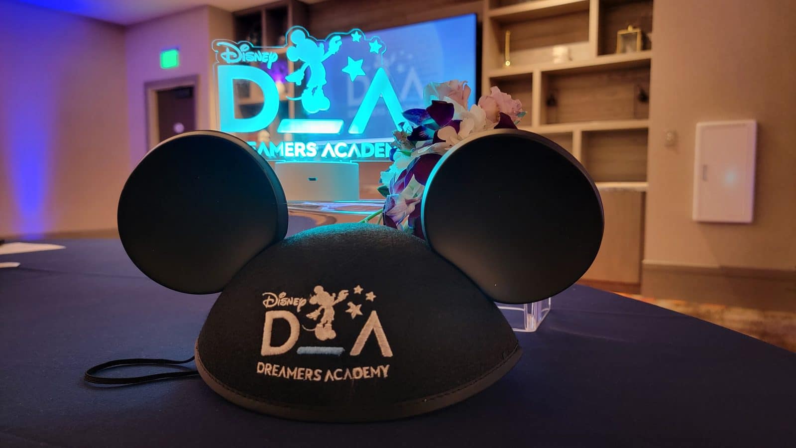 Disney Dreamers Academy ear headband on a table with a blue neon sign displaying the event name in the background