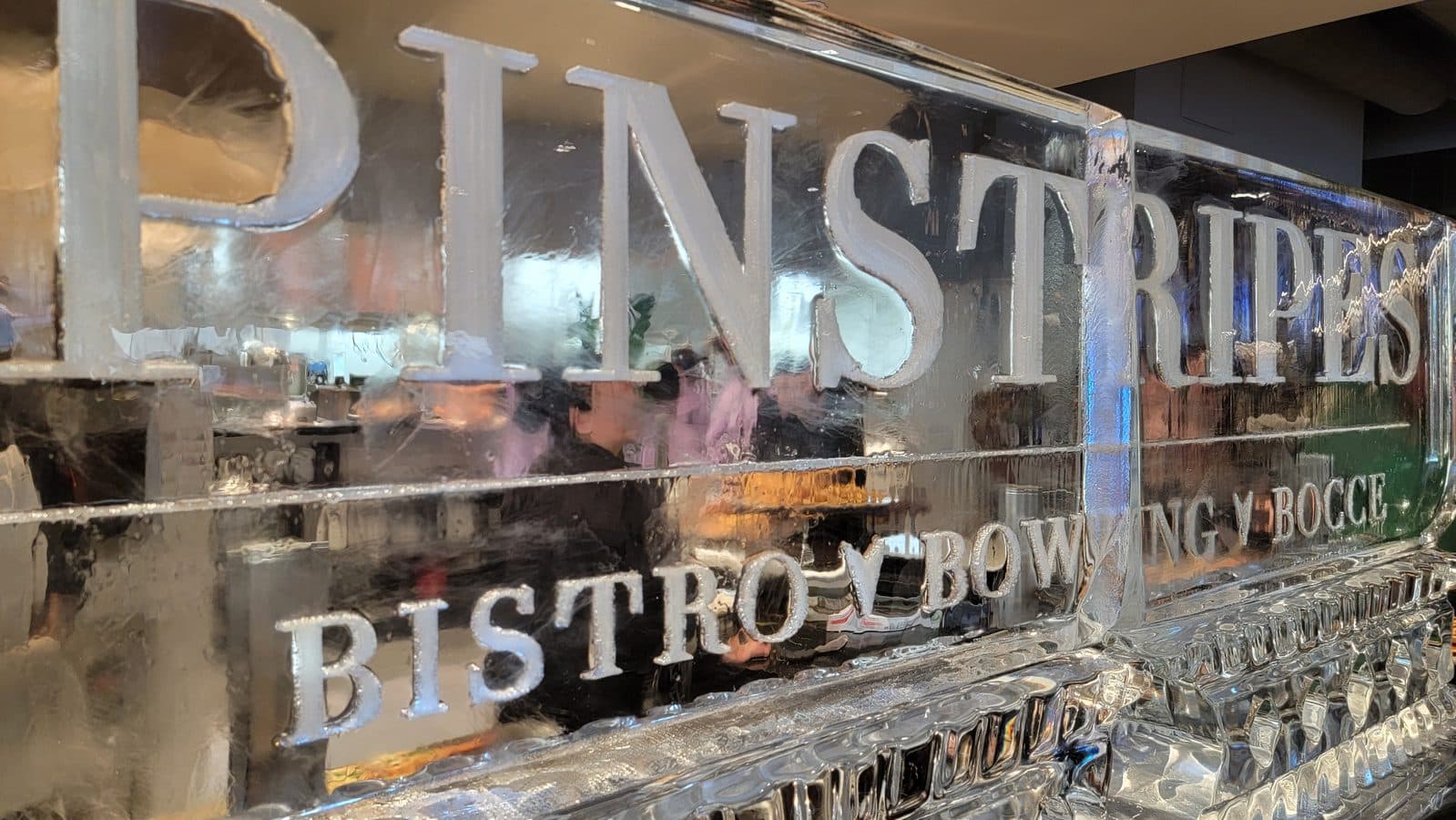 Close up of a polished chrome sign with large raised lettering reflecting a showroom and blurred figures in the background