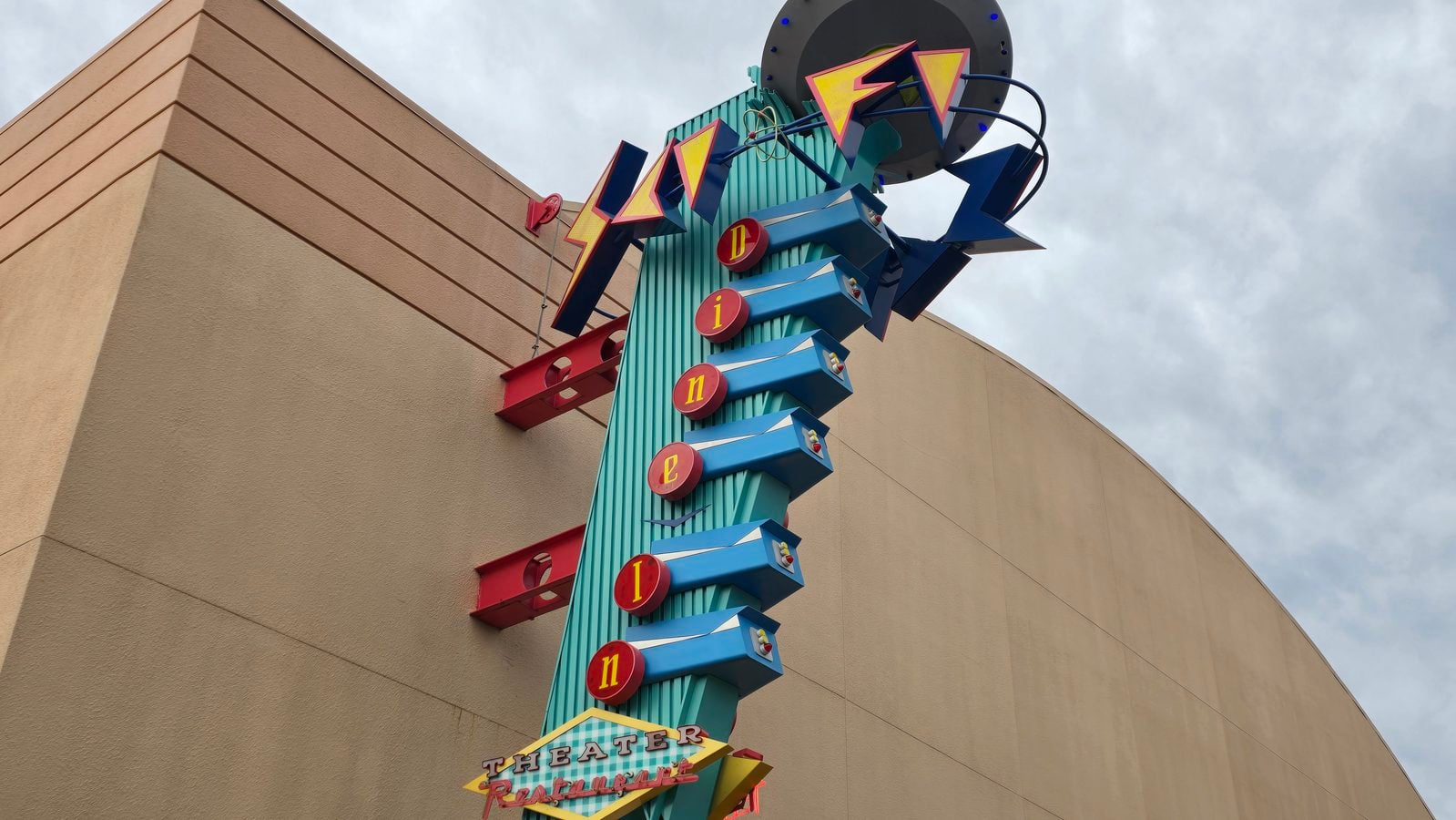 Colorful retro theater sign mounted on a turquoise column against a beige wall reading theater with arrow like shapes and letters