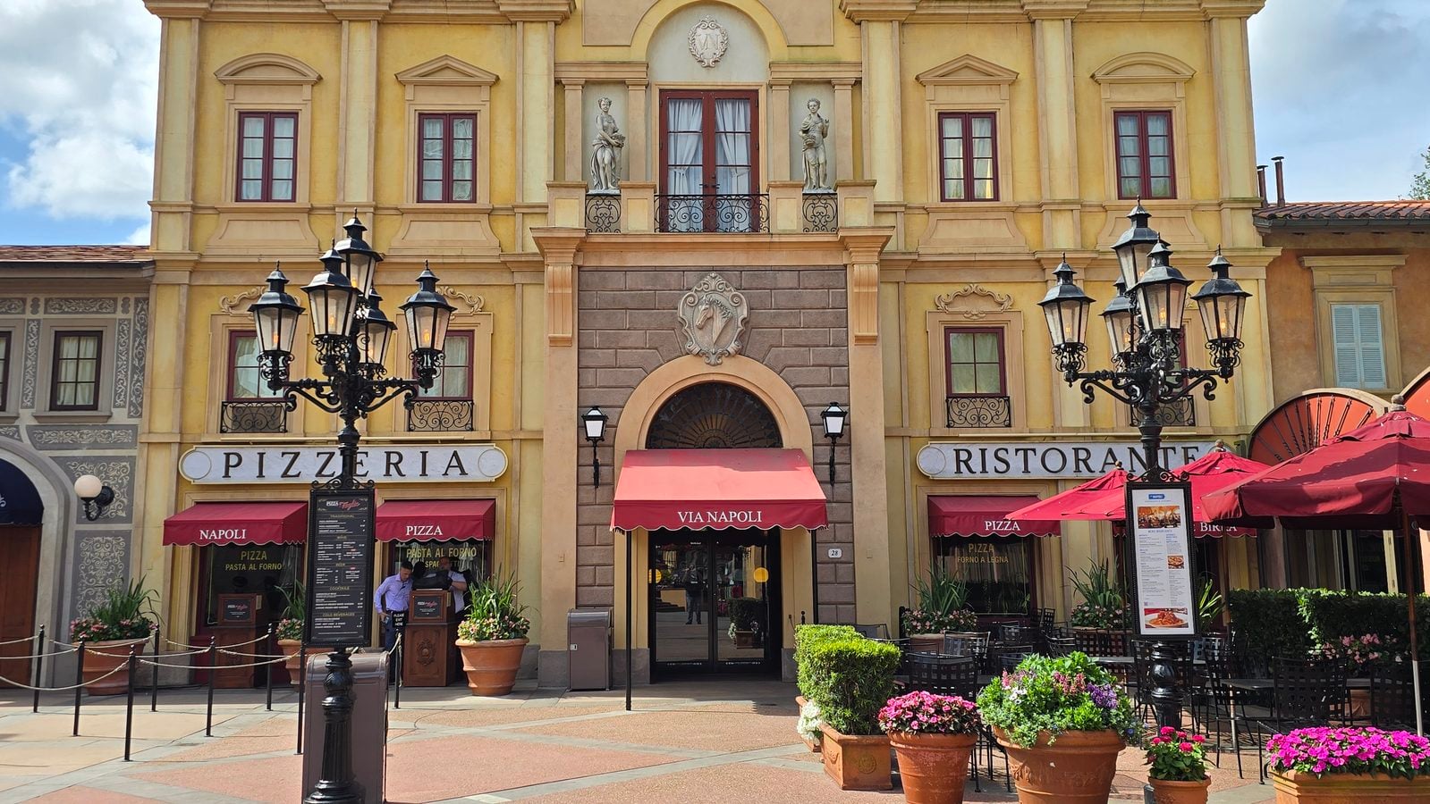 Facade of a Mediterranean style building with pizzeria and ristorante signs red awnings and outdoor seating under decorative lamps