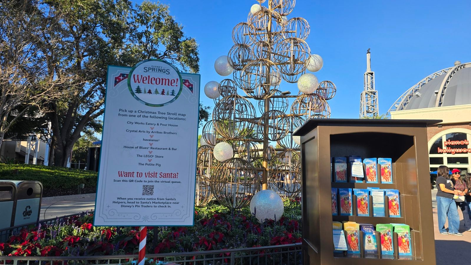 Disney Springs Welcome sign beside a metallic spherical holiday sculpture and a brochure kiosk nearby