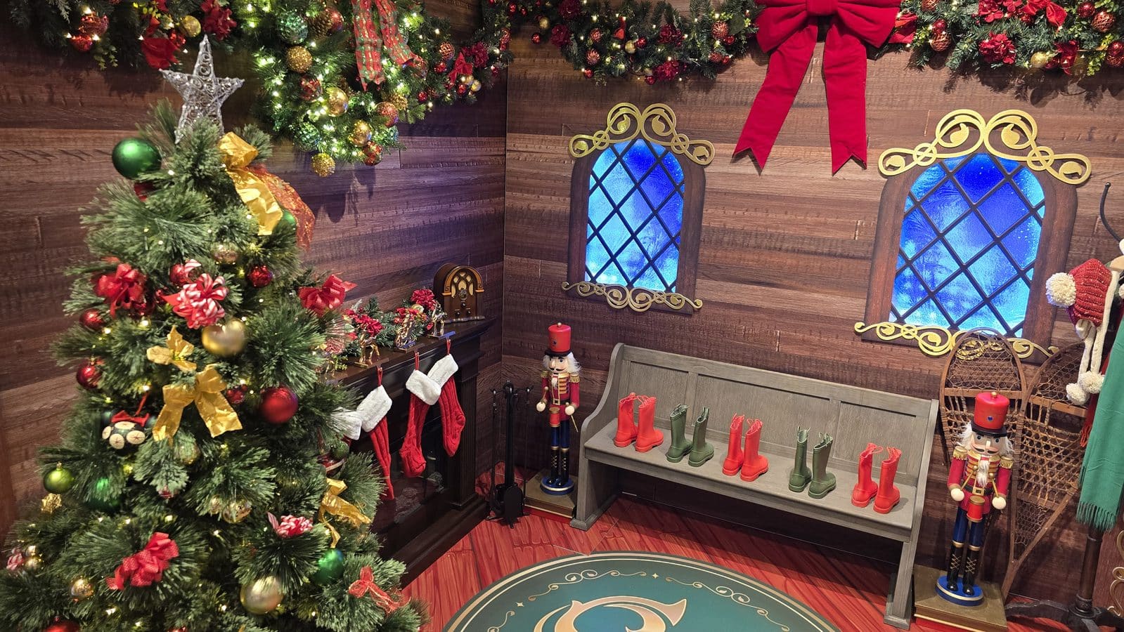 Decorated Christmas scene with a tall tree garlands stockings and colorful boots on a bench beside nutcrackers and a faux medieval window wall