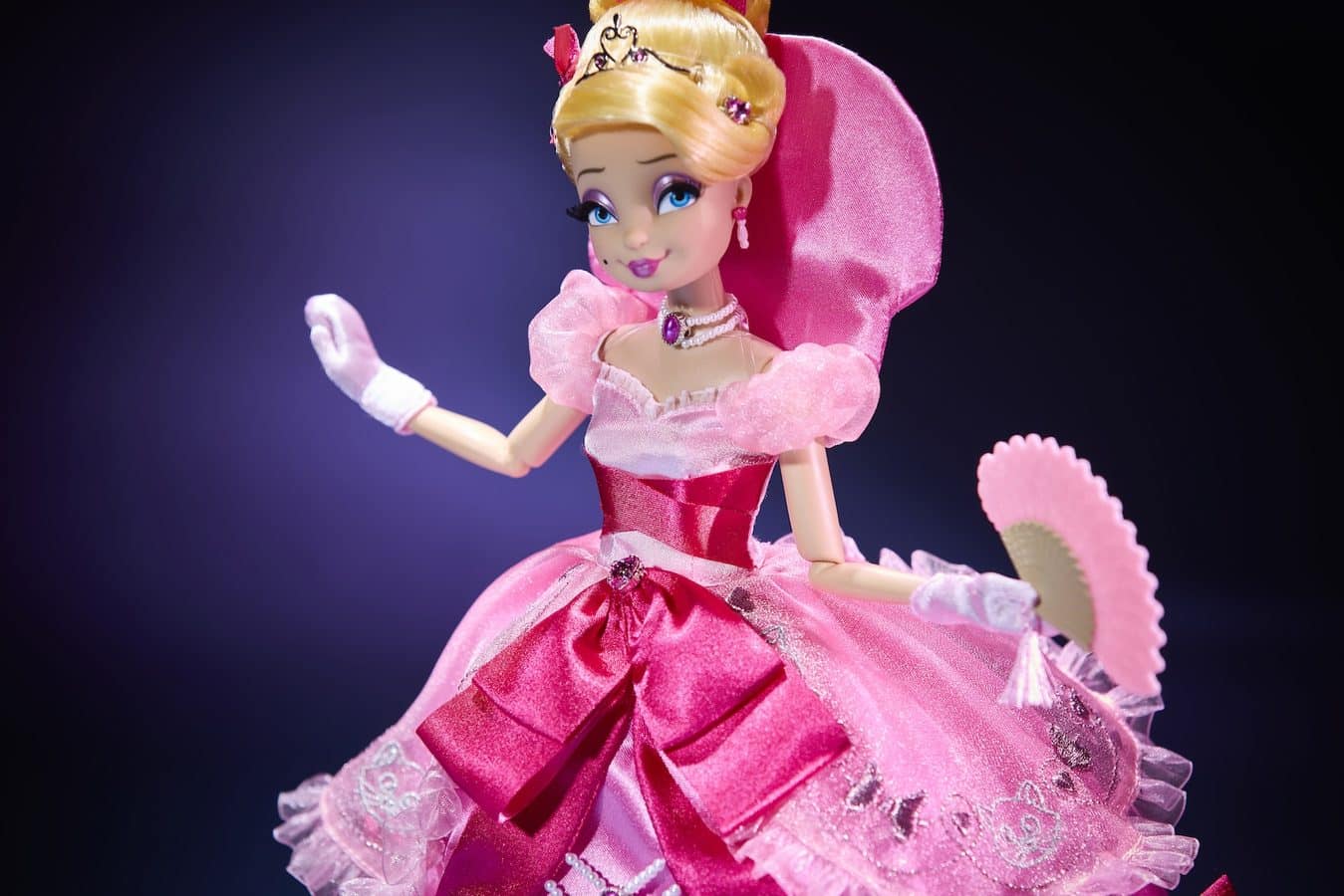 Pink princess doll in a sparkling gown with a tiara and pink fan against a dark background