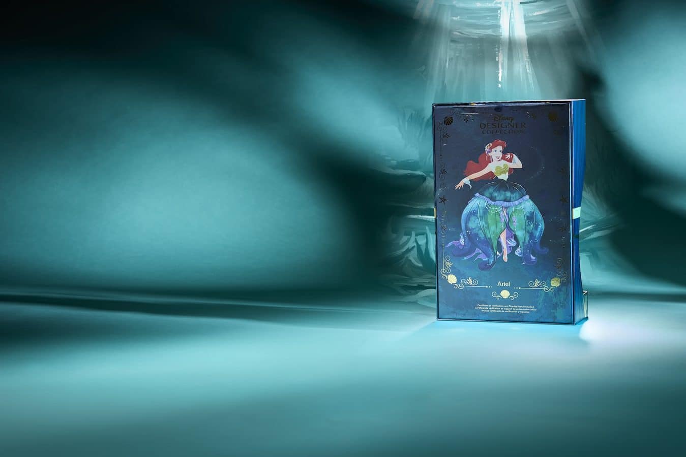 Blue Disney Designer Collection box featuring Ariel from The Little Mermaid with a red haired Ariel in a green bodice and teal skirt on a teal lit surface