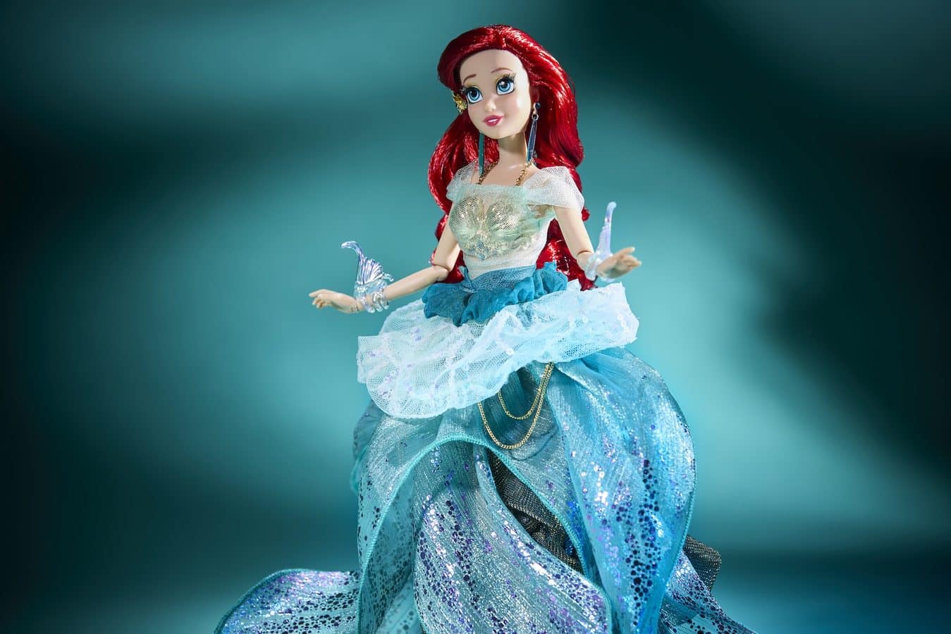 Toy doll with bright red hair in a sparkling blue gown posed against a teal gradient background