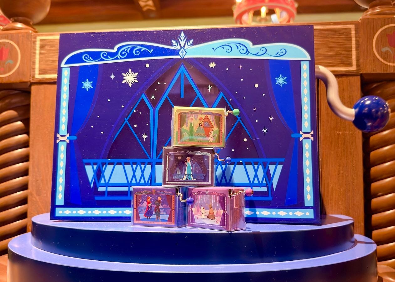 Blue decorative display featuring a dark blue stage backdrop with diamond window shapes and a stack of illustrated story cards on a round blue pedestal