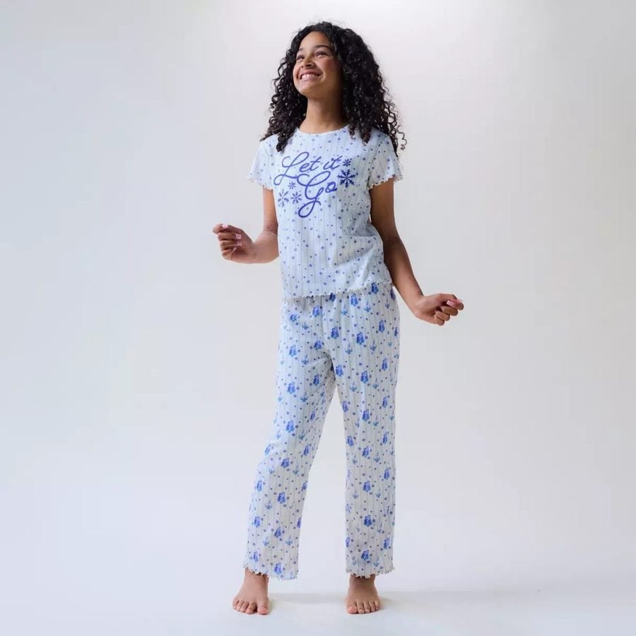 Smiling woman with curly hair wearing a light blue floral pajama set barefoot with the shirt reading Let it Go and snowflake accents
