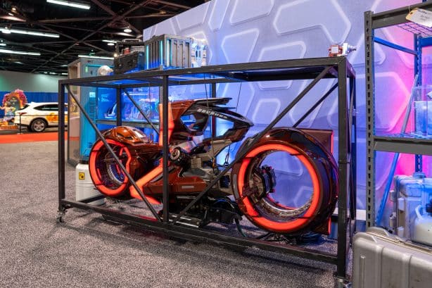 Red futuristic motorcycle inside a black metal display cage at a convention center exhibition floor