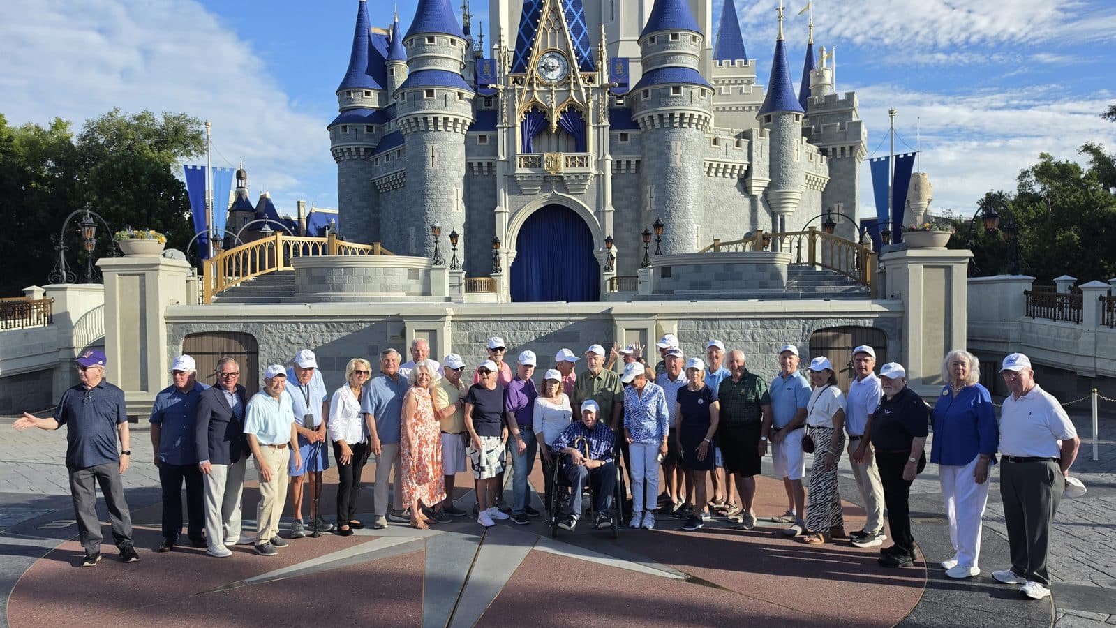 Large group of adults and seniors posing for a photo in front of a blue roofed castle at a theme park