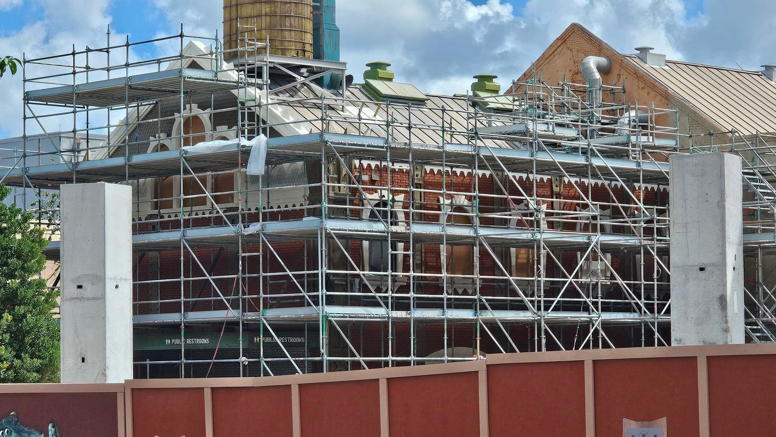 Building under renovation surrounded by metal scaffolding covering a brick facade with decorative arches and a blue sky above