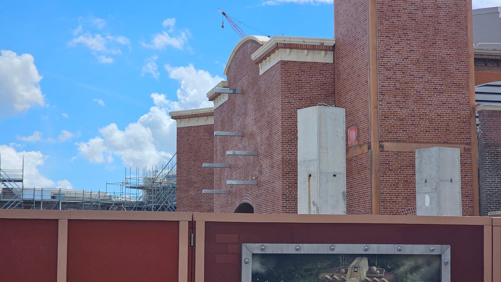 Construction site with red brick walls scaffolding and a distant crane against a bright blue sky with white clouds