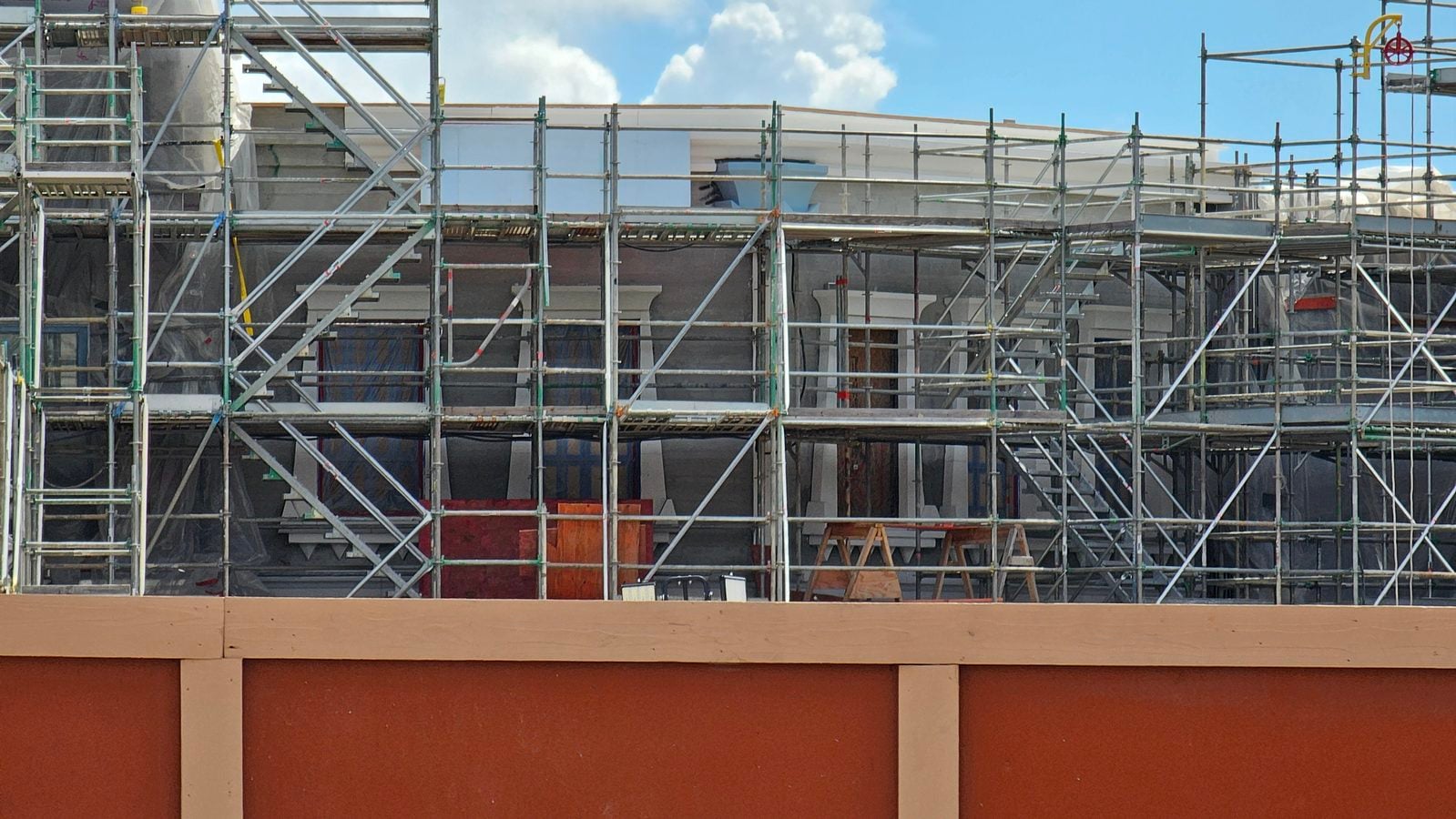 Construction scaffolding covers a building under renovation against a blue sky The orange wall is visible at the bottom