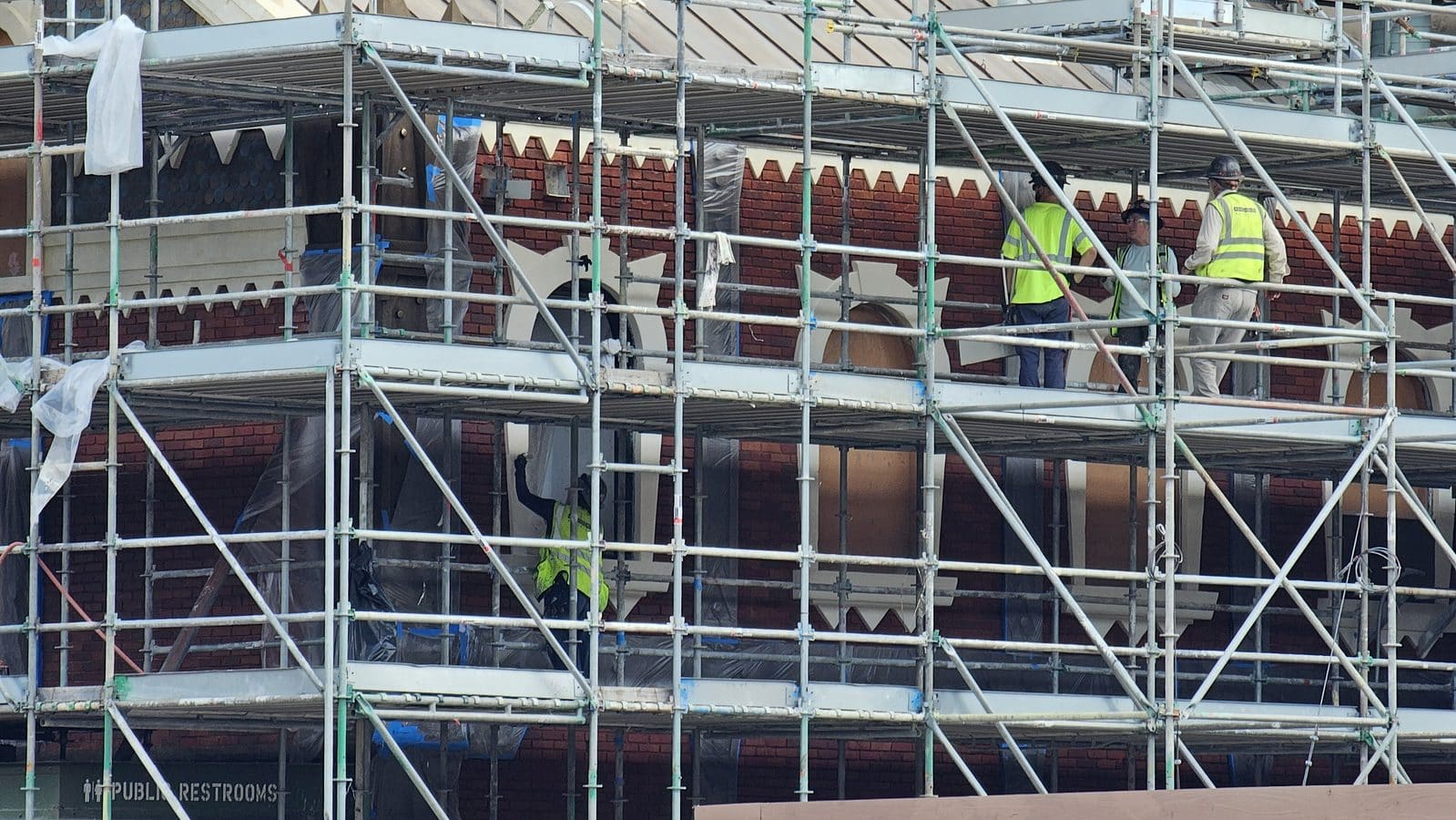 Construction workers in high visibility vests and hard hats on scaffolding around a brick building under renovation