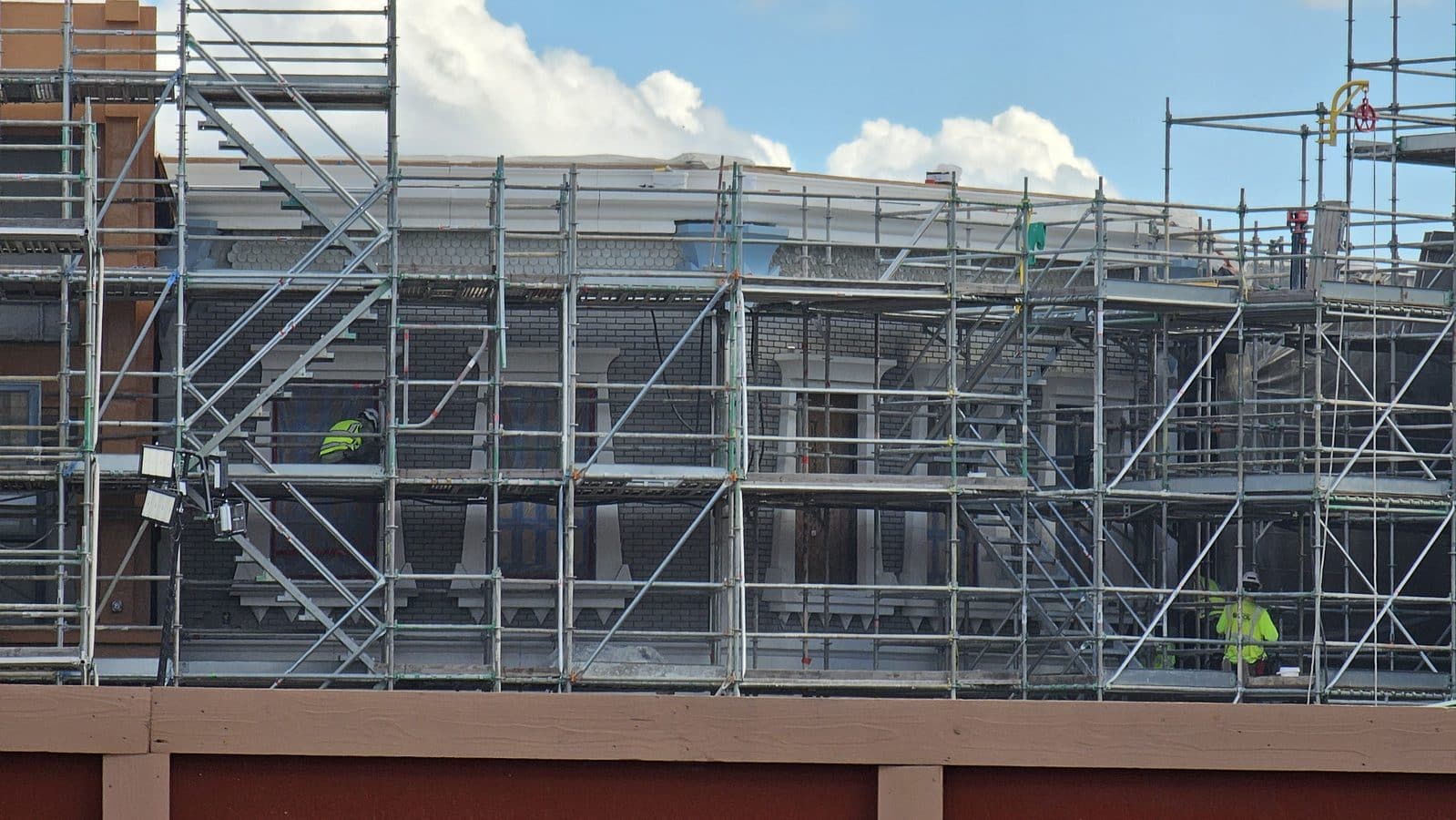 Construction site with metal scaffolding around a brick building under a blue sky
