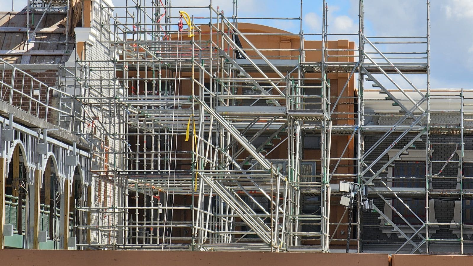 Extensive metal scaffolding surrounds a brick building under construction on a sunny day