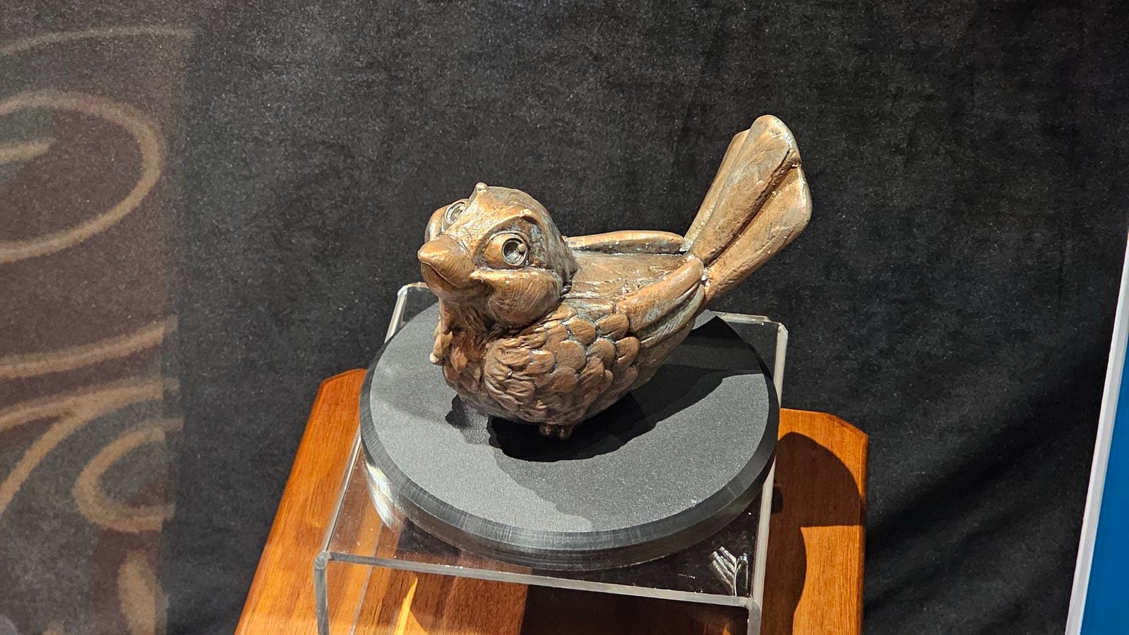 Wooden fish sculpture with big eyes on a black display pedestal in a gallery setting
