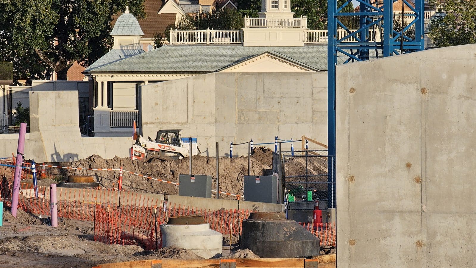 Blue tower crane over a flooded trench with wood shoring and a green pump at the Piston Peak construction site