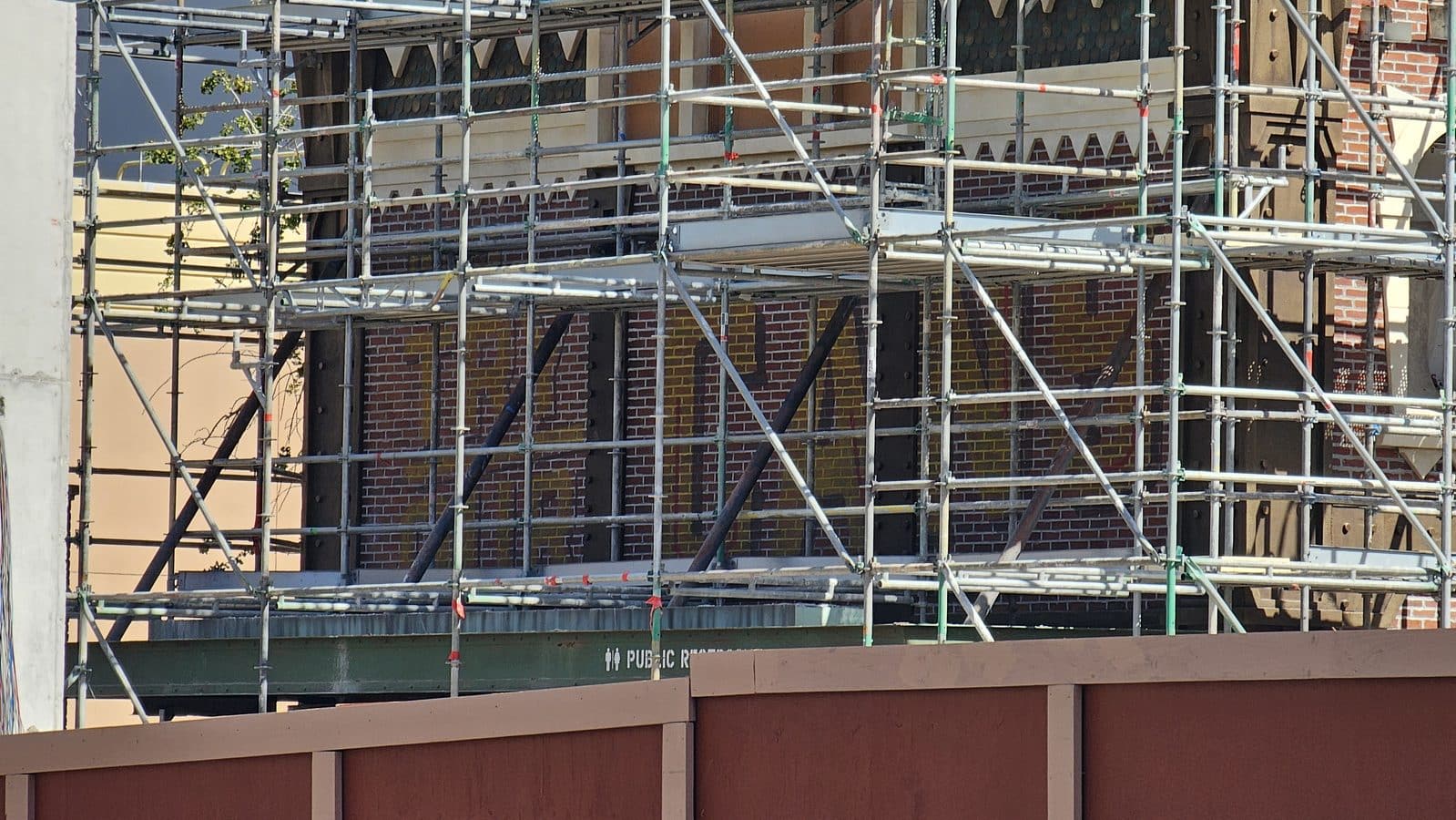 Exterior of a brick building under renovation wrapped in multilevel metal scaffolding a public access sign is visible on the storefront at the bottom