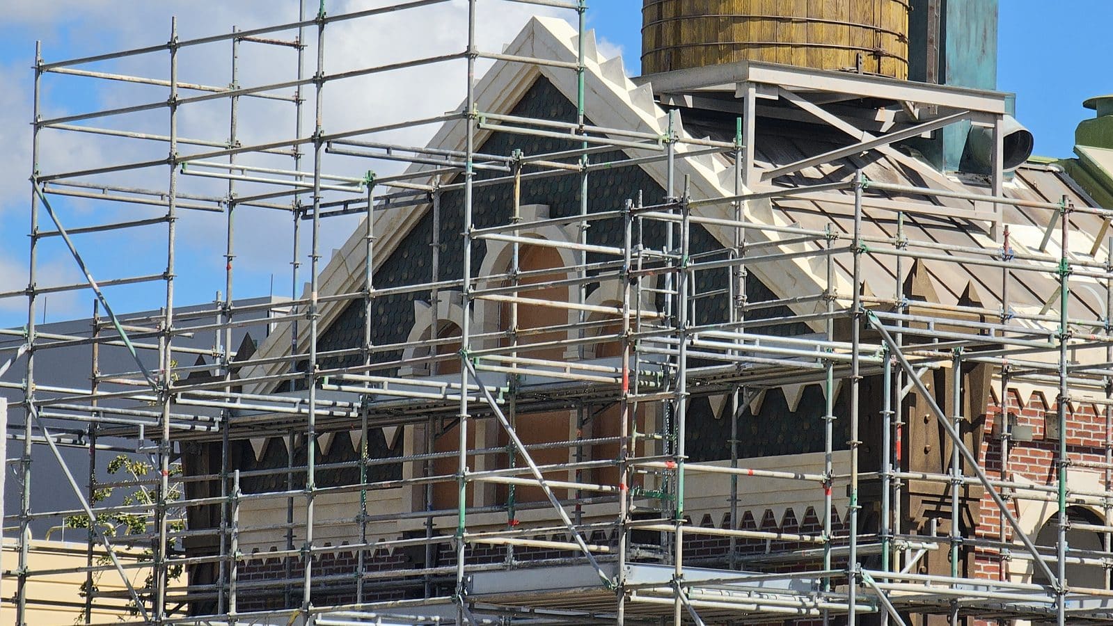 Metal scaffolding surrounds a brick building with a steep decorative gable roof under renovation blue sky in the background