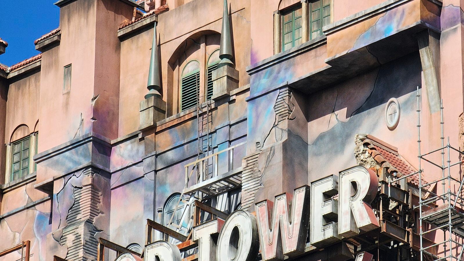 Pink stucco building facade covered in a pastel mural with arched windows and decorative spires