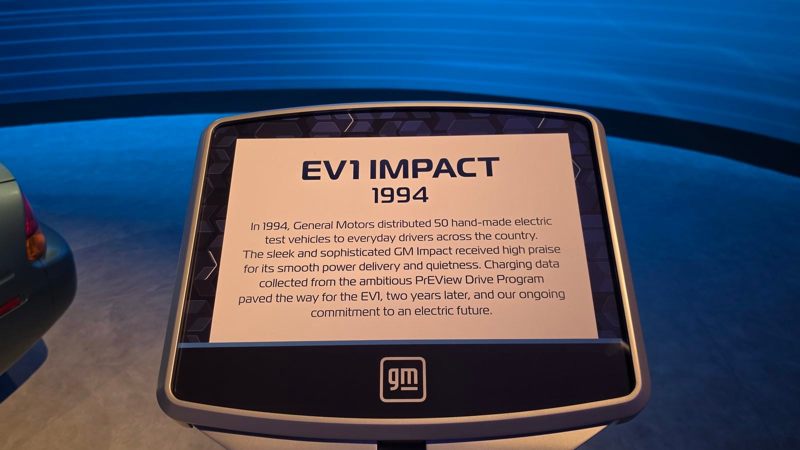 Informational placard on an EV1 display titled EV1 IMPACT 1994 with descriptive text and a GM logo nearby