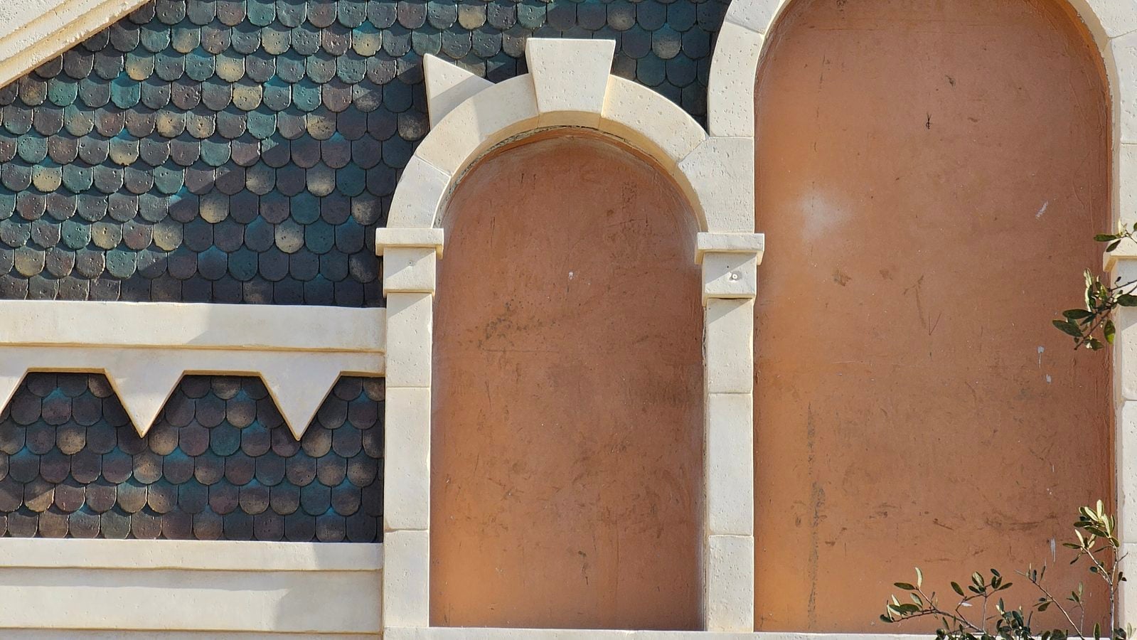 Close up of decorative white arches framing brown stucco panels on a teal tiled roof