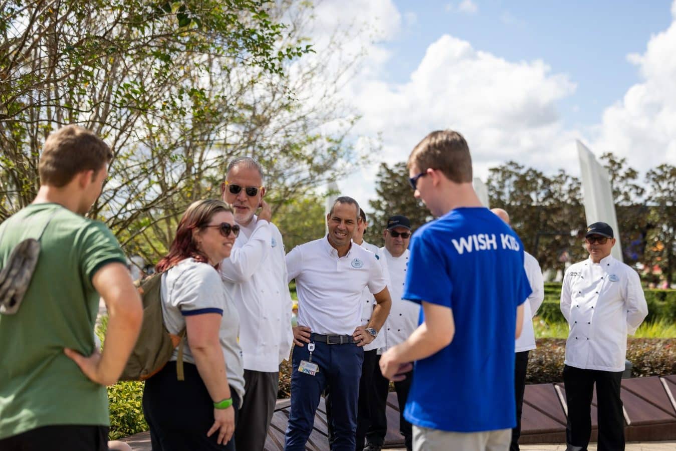 Group of volunteers outdoors a man in a blue WISH KID shirt talks with others in white shirts