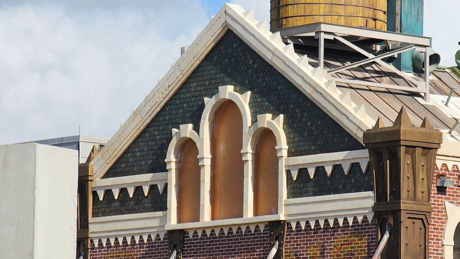 Front gable of Archie's Scare Pig Pizza in Monstropolis with three arched windows, horned trim, rows of teeth and a wooden water tower on the roof