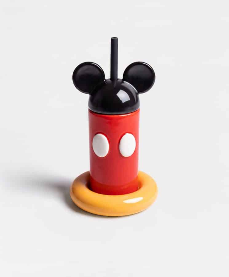 Red drinking bottle with a black Mickey Mouse head cap and straw resting on a yellow base