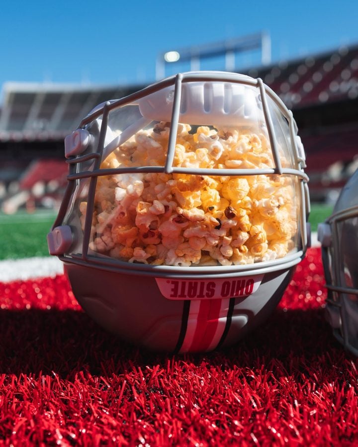 Close up of a helmet filled with popcorn on a football field with blurred stadium seats in the background