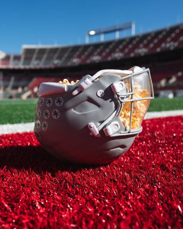 Close up of a popcorn bucket resting on red stadium turf with blurred stands in the background under a clear blue sky