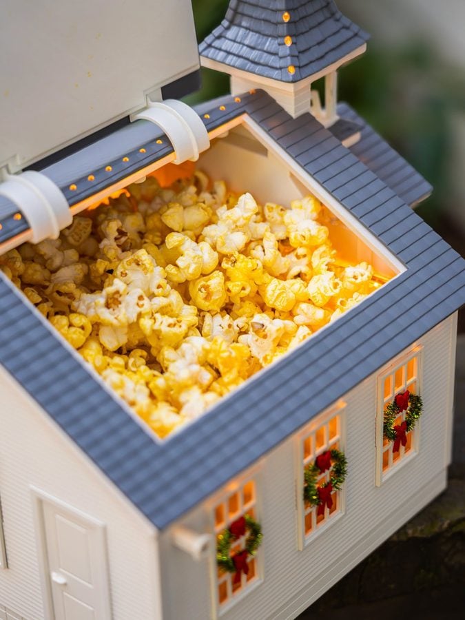 Miniature dollhouse with a blue roof warm lights in windows and popcorn filling the attic area holiday wreaths on the front doors below