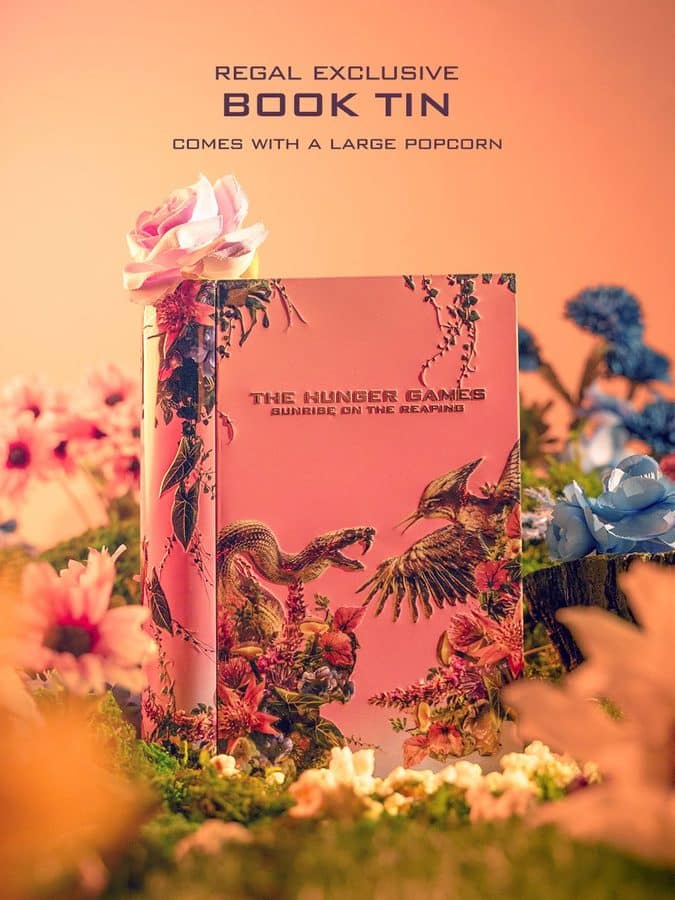 Pink tropical themed Hunger Games book tin displayed among colorful flowers header text reads Regal Exclusive Book Tin and comes with a large popcorn