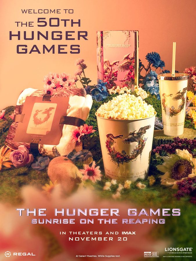 Promotional Hunger Games poster with a decorative still life popcorn tub tumbler bouquet of flowers and a book all themed with Hunger Games imagery text reads The Hunger Games Sunrise on the Reaping and November 20
