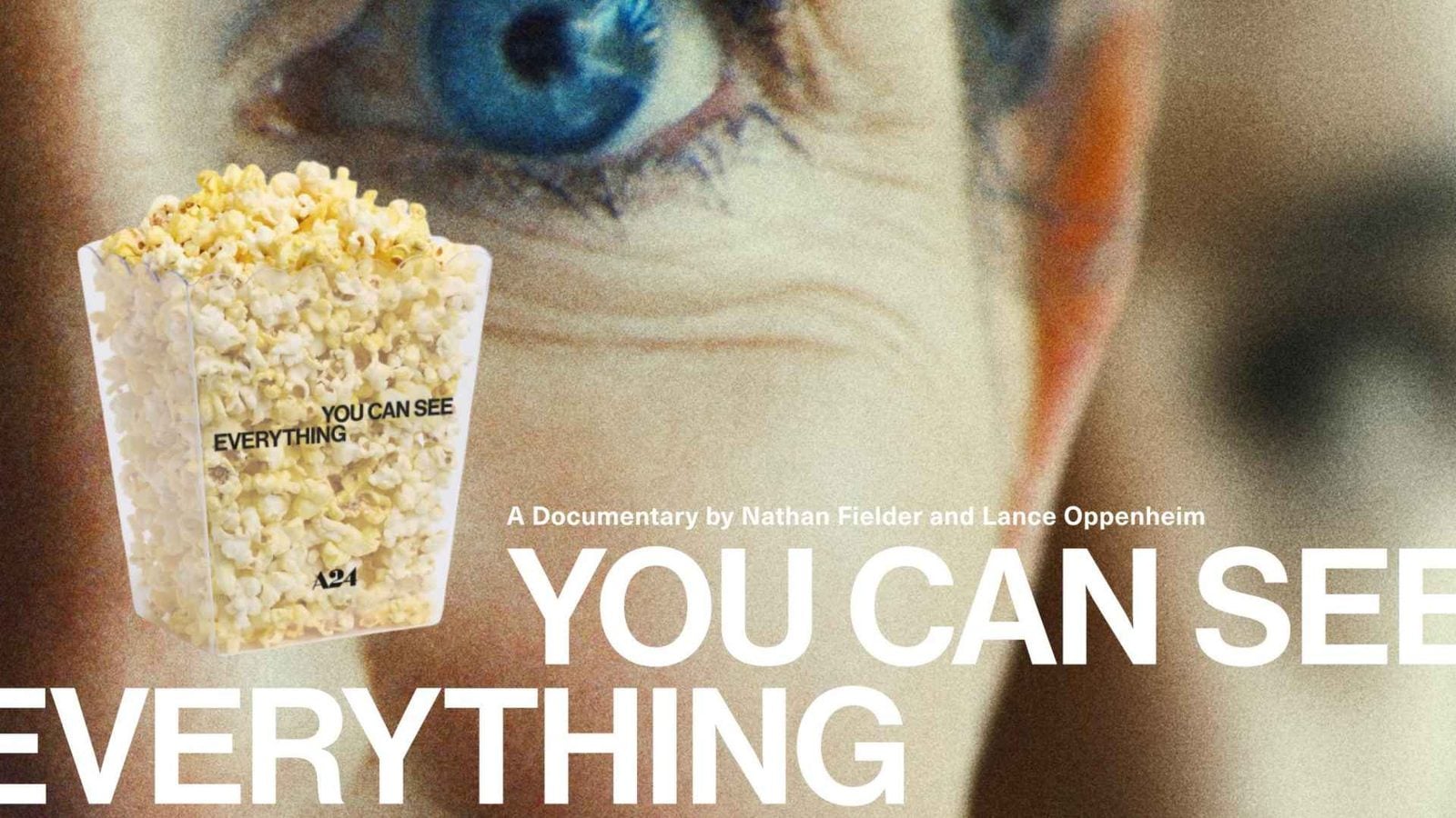 Close up of a white popcorn tub held up with large white text from a documentary poster in the background reading YOU CAN SEE EVERYTHING
