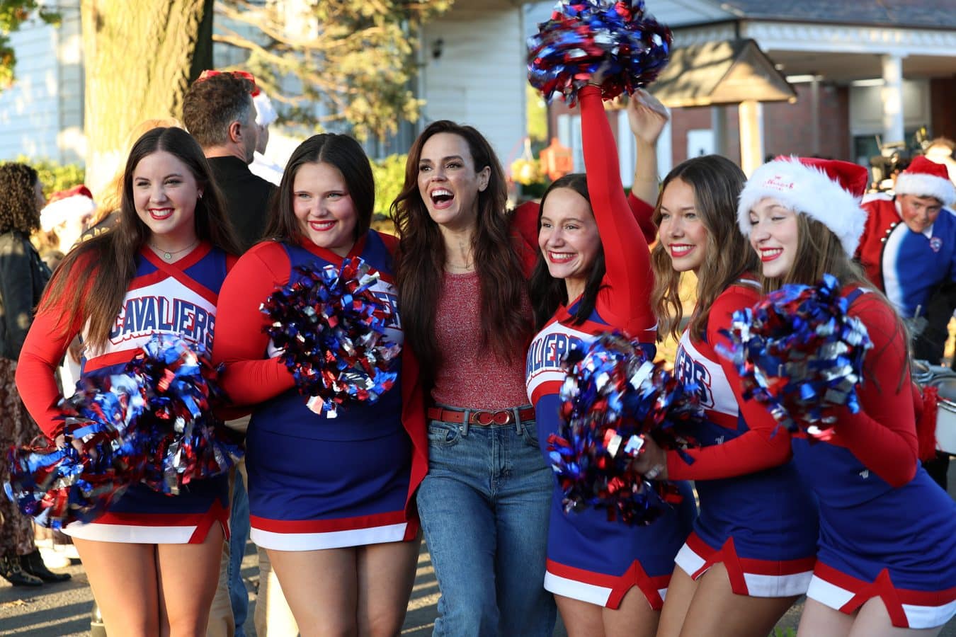 Smiling group of cheerleaders in red white and blue uniforms waving blue red pom poms at an outdoor parade